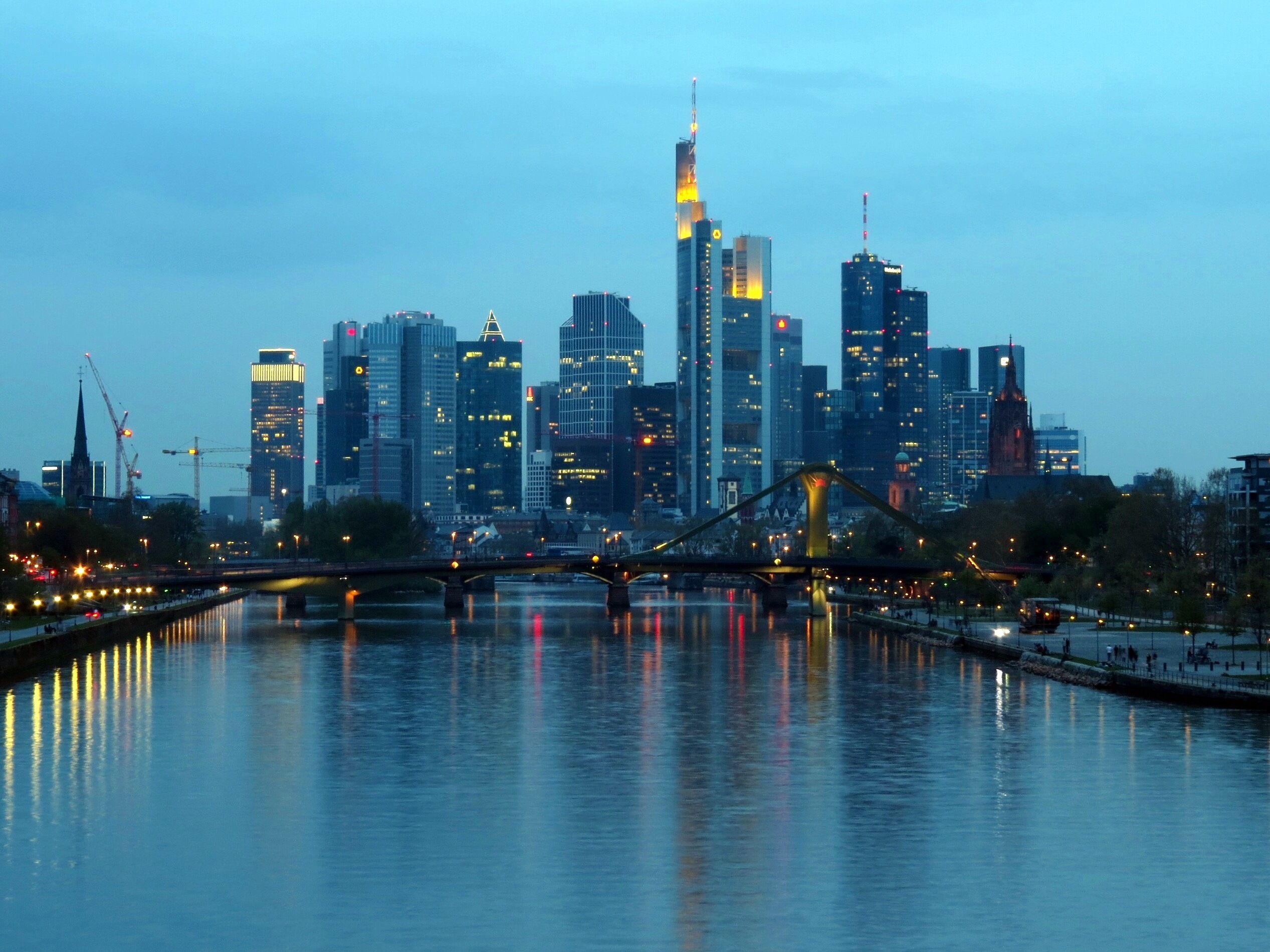 Een stadshemelbeeld in de schemering met een rivier op de voorgrond en een brug erover.