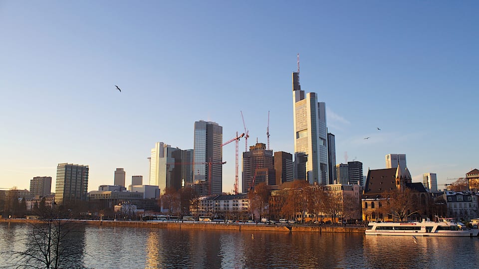 Une vue sur les toits d’une ville, avec des gratte-ciel modernes, une rivière et un bateau.
