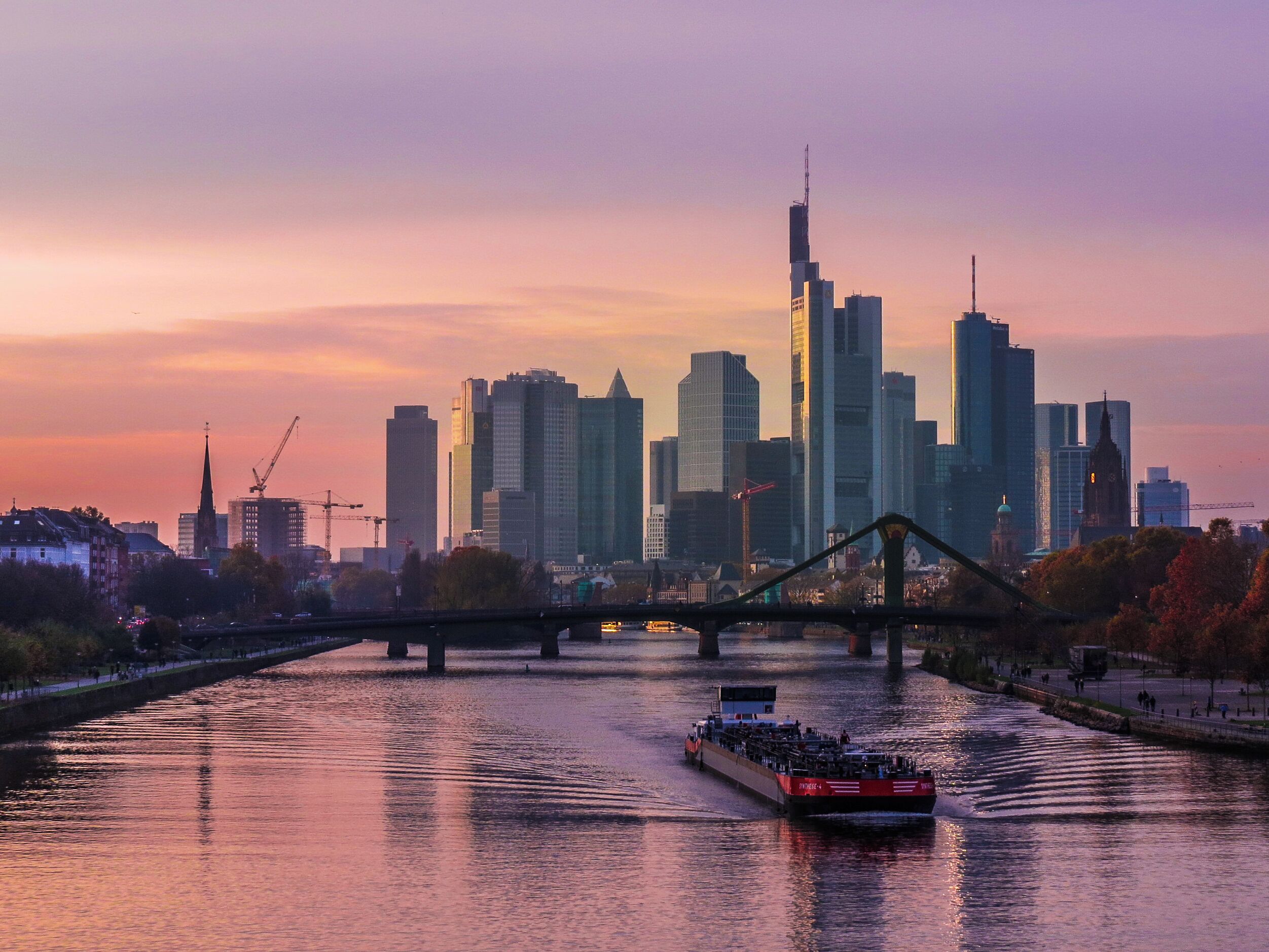 A river with a boat, a bridge, and a city skyline with tall buildings.