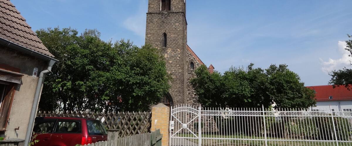 A tall church tower with a clock, surrounded by trees and a fence.