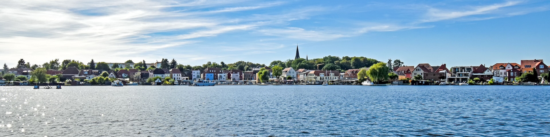 A riverside town with historic buildings, a church spire, and boats on the water.
