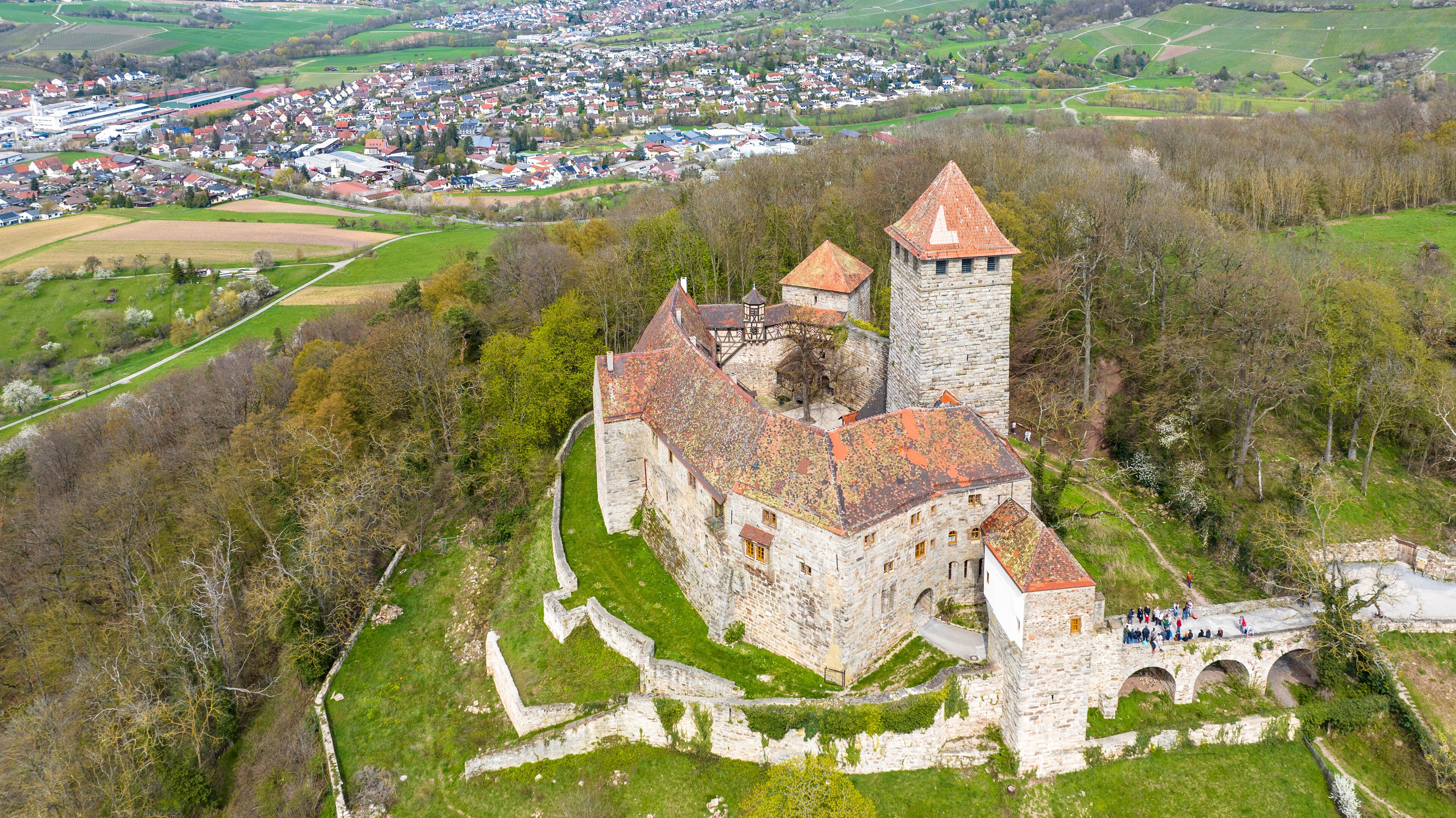 An aerial view of a historic castle surrounded by lush greenery and a small village in the background.