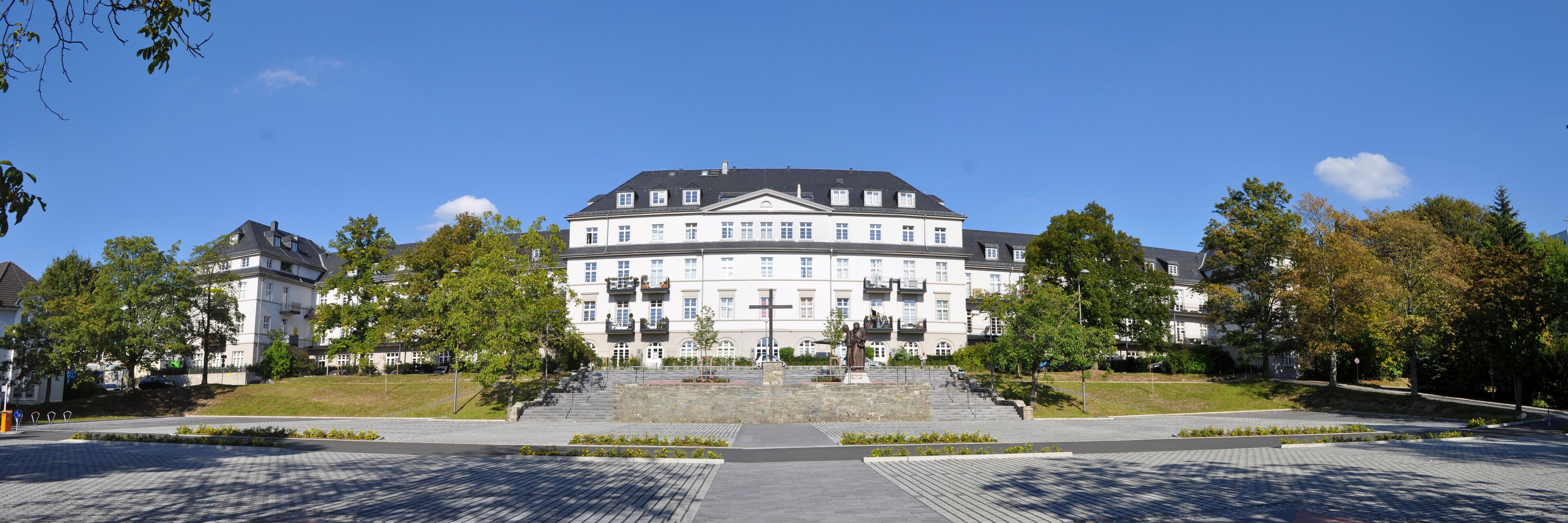 A large, historic building with a central staircase and a statue in front.