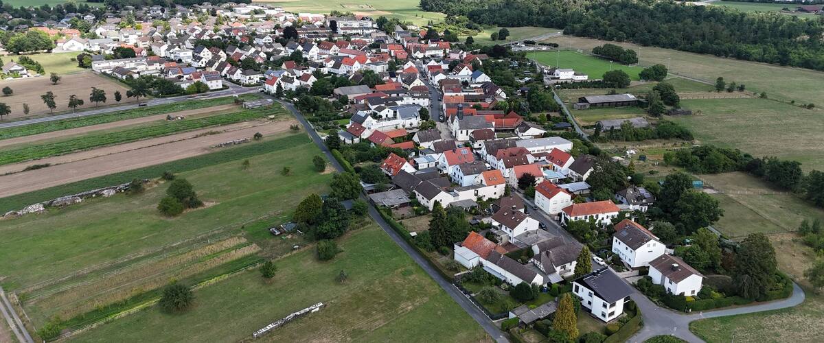 An aerial view of a residential area with houses, green fields, and a distant power plant.