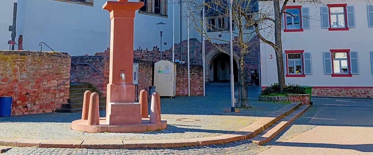 A church with a tall tower and a clock, a stone well, and a building with red window frames.