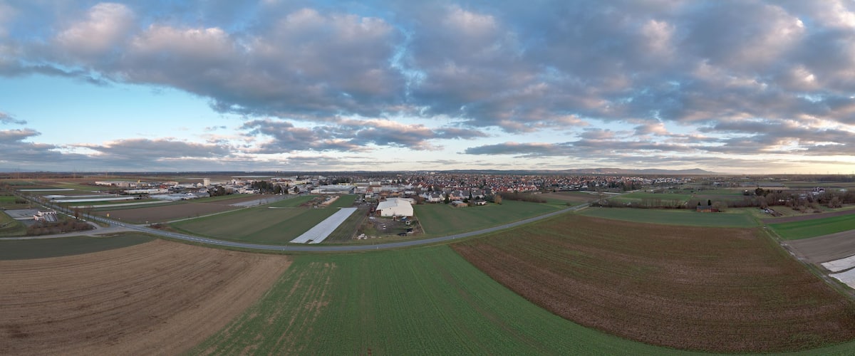 An aerial view of a town with fields, roads, and a cloudy sky.