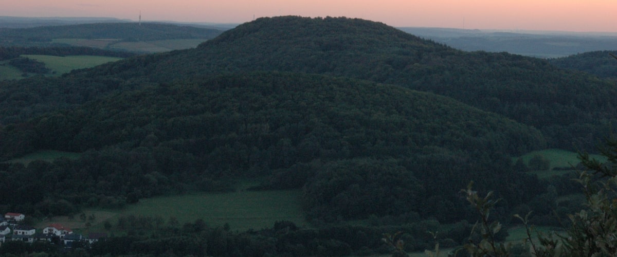 A hilly landscape with a hill in the foreground and a flat area with buildings in the distance.