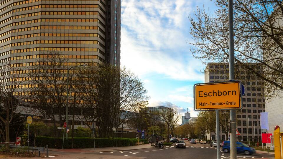A street with a sign reading 'Eschborn Main-Taunus-Kreis,' buildings, and a clear sky.