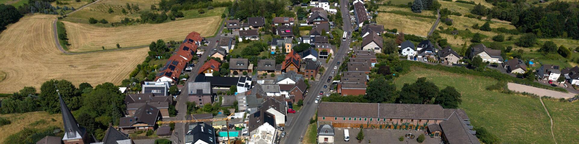 An aerial view of a small town with a mix of residential houses, a church, and a large industrial building.