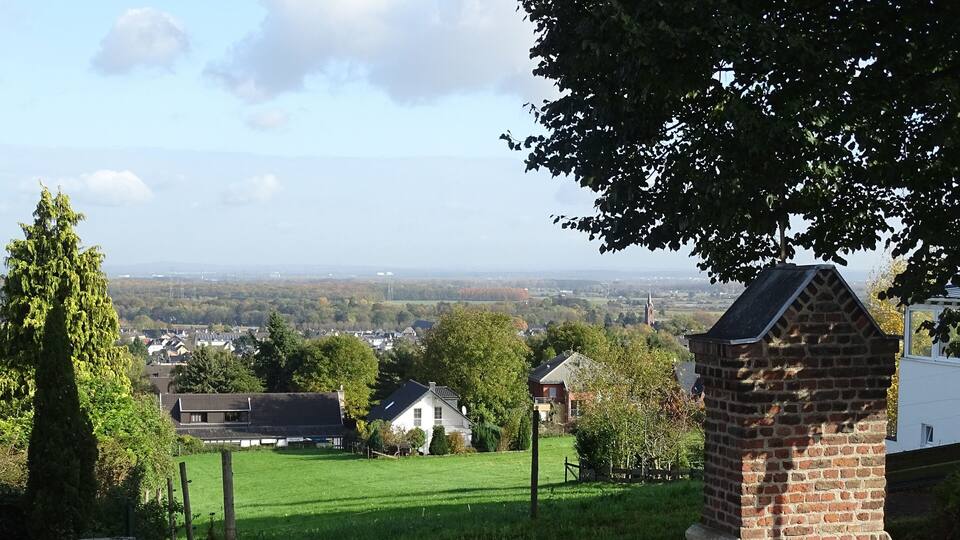 A rural landscape with a grassy field, a brick structure, and houses in the background.