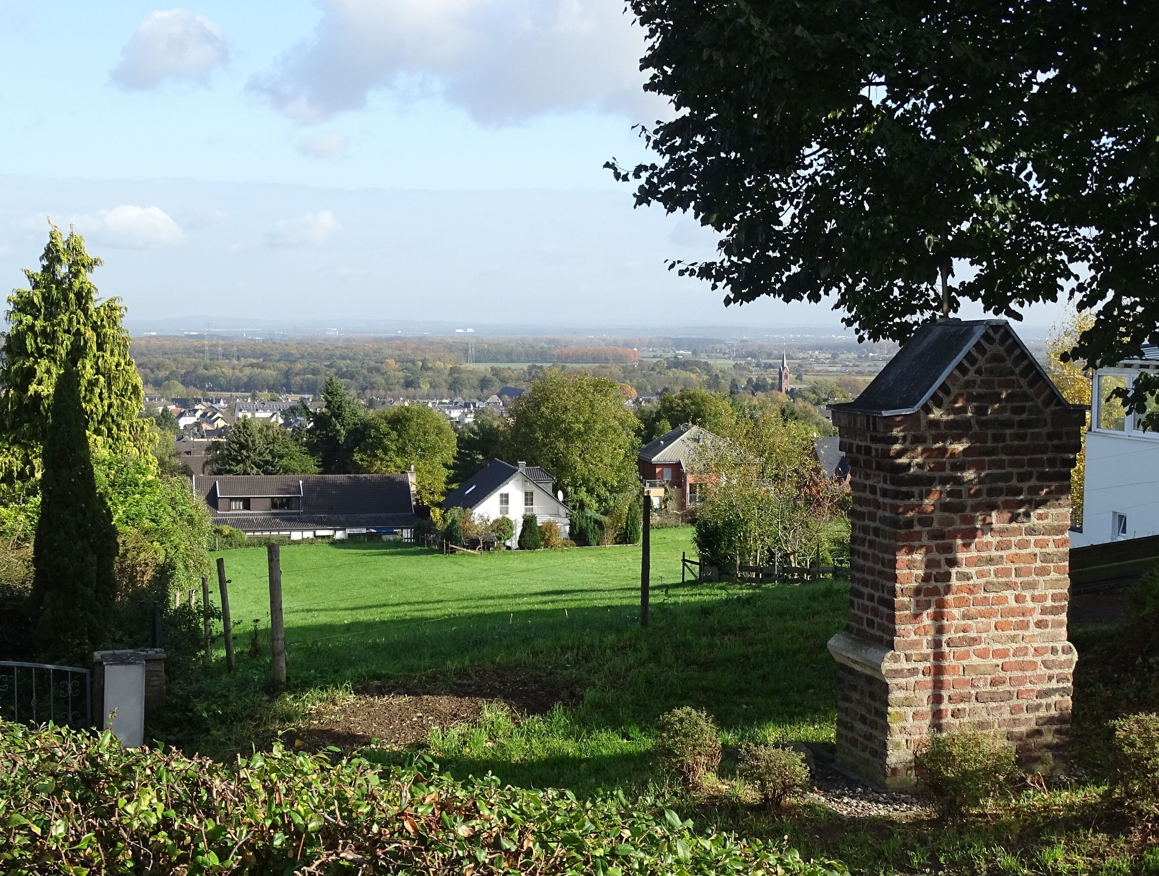 A rural landscape with a grassy field, a brick structure, and houses in the background.