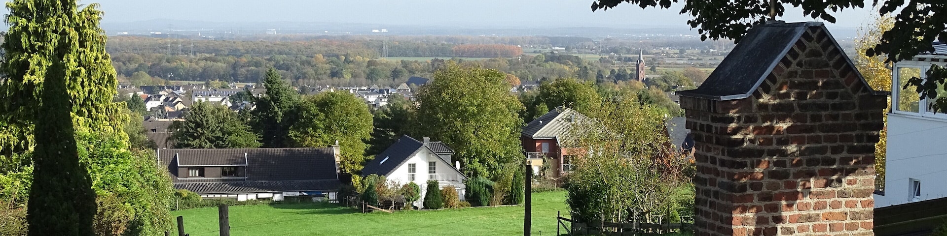 A rural landscape with a grassy field, a brick structure, and houses in the background.