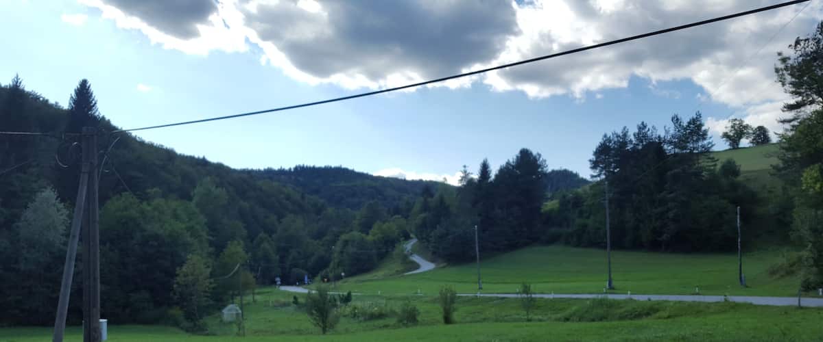 A green valley with a winding road, power lines, and a forested hill in the background.