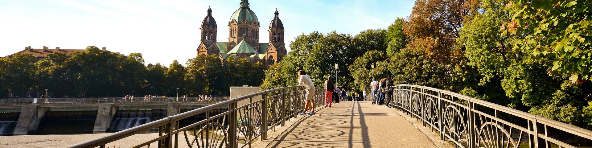 A bridge with ornate railings, a river, and a historic building with domes in the background.