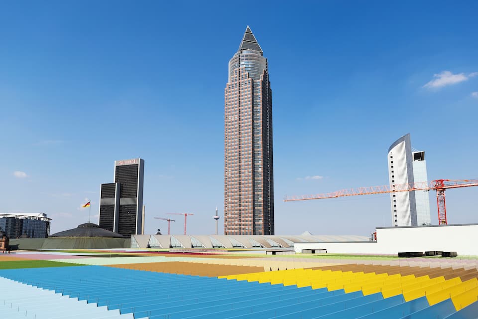 A modern cityscape with a prominent skyscraper, a stadium, and construction cranes.