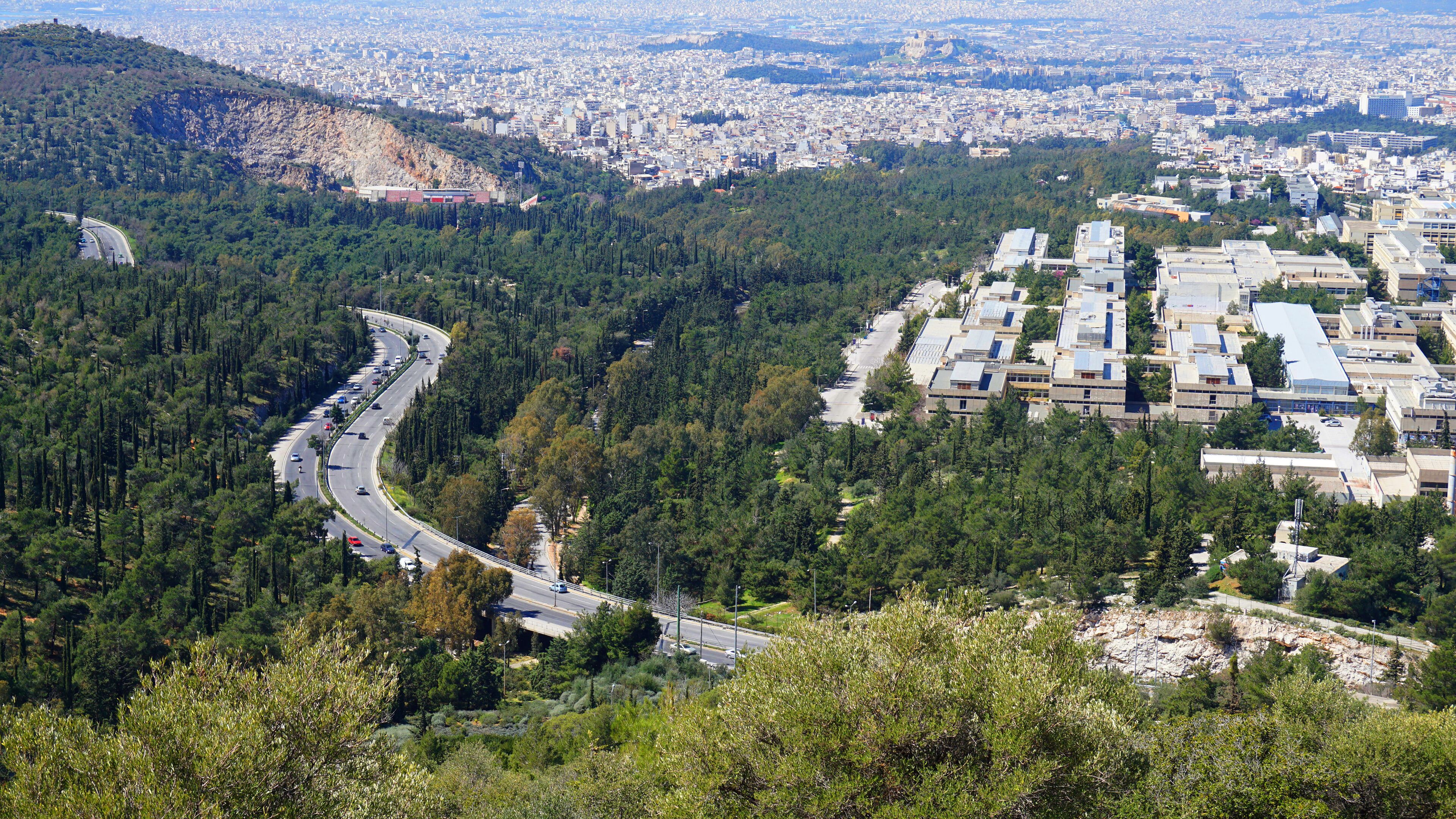 A winding road through a forested area with a city in the background.