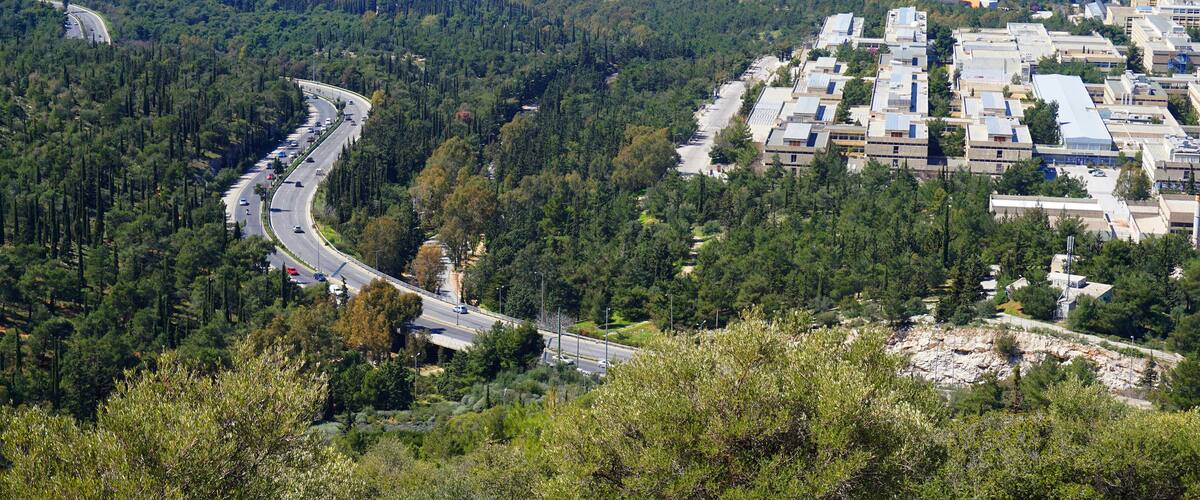 A winding road through a forested area with a city in the background.
