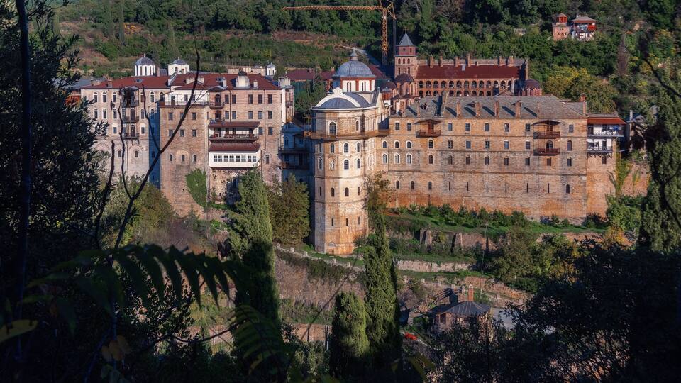 A historic castle complex with multiple towers and domed structures, surrounded by lush greenery and hills.