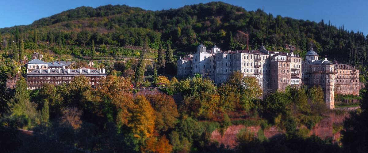 A historic castle complex with multiple buildings, surrounded by dense forest and hills.