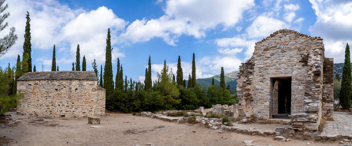 An ancient stone structure with a stone door and a small building with a tiled roof, surrounded by trees and mountains.