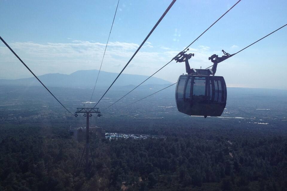 A cable car suspended above a forested landscape with a clear sky and distant mountains.