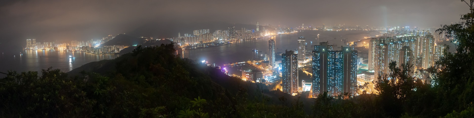 Paisagem urbana noturna com arranha-céus, um rio e uma ponte.