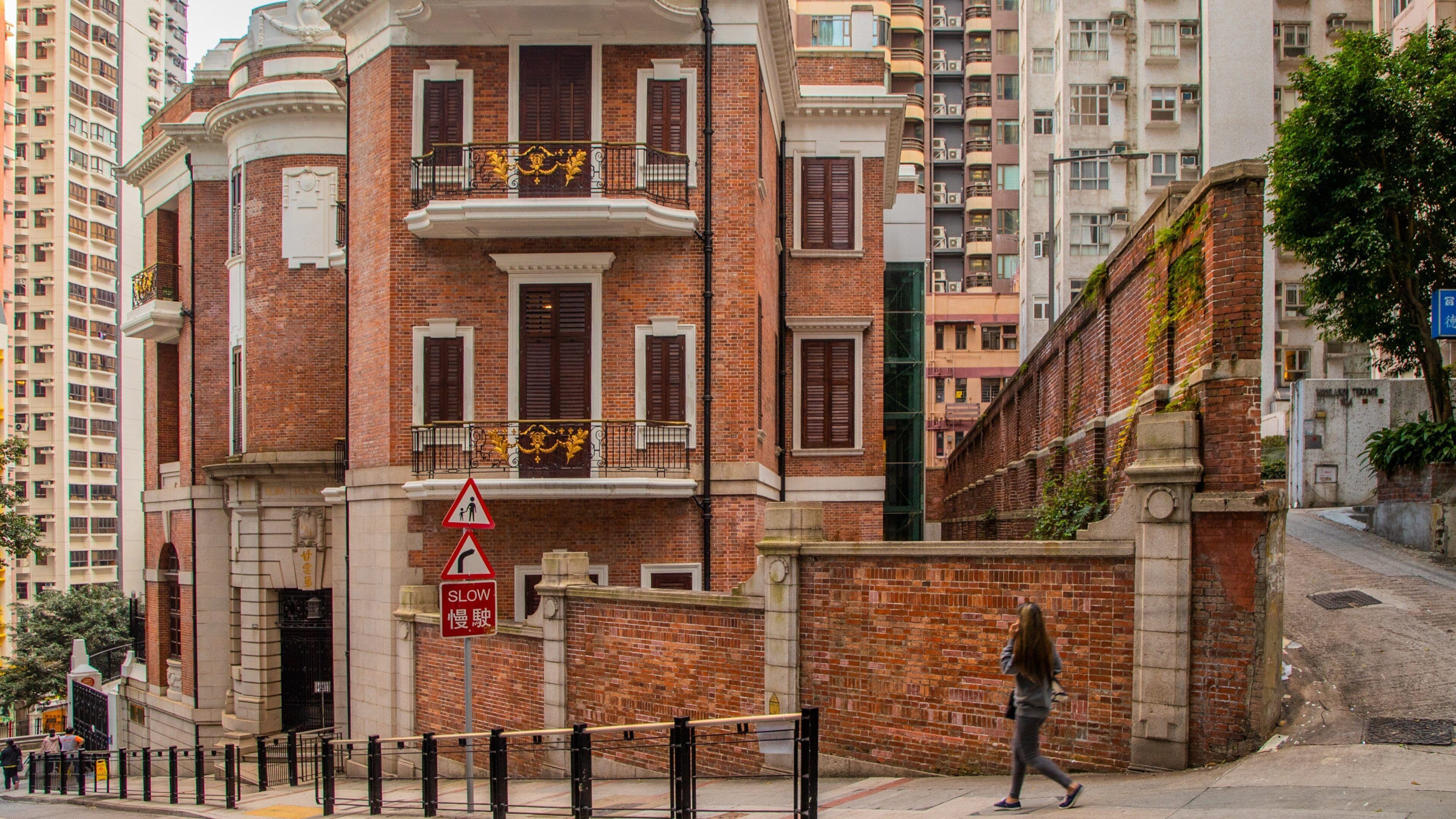 Ein historisches Gebäude mit roten Backsteinfassaden, einem Balkon mit aufwendiger Metallgitterverzierung und einem Fußgängerüberweg-Schild.