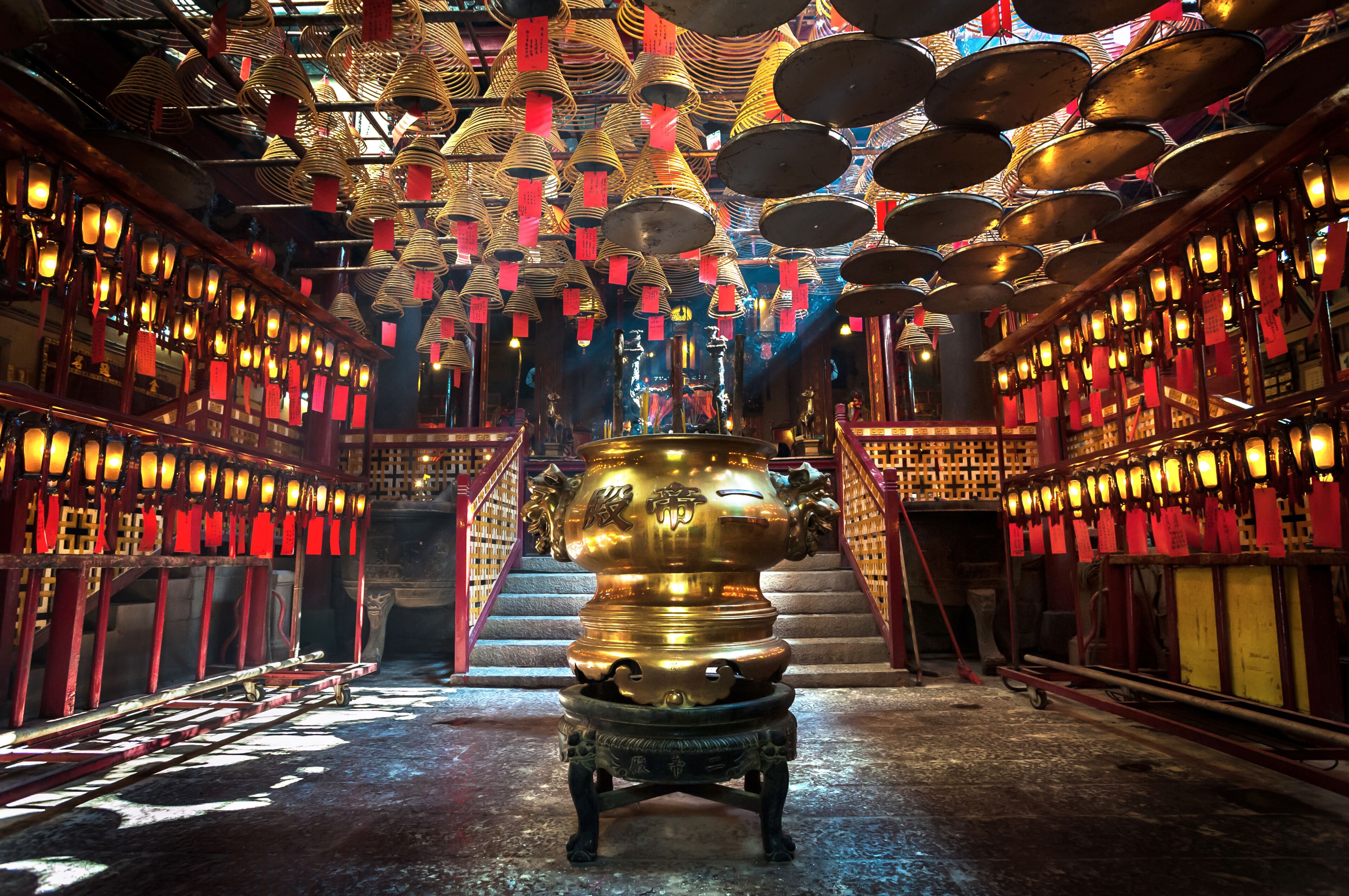 A temple interior with golden statues, red lanterns, and a central incense burner.