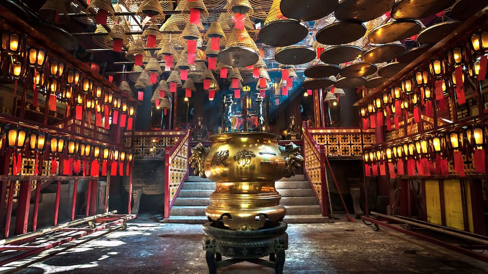 Interior de un templo con estatuas doradas, faroles rojos y un quemador de incienso en el centro.