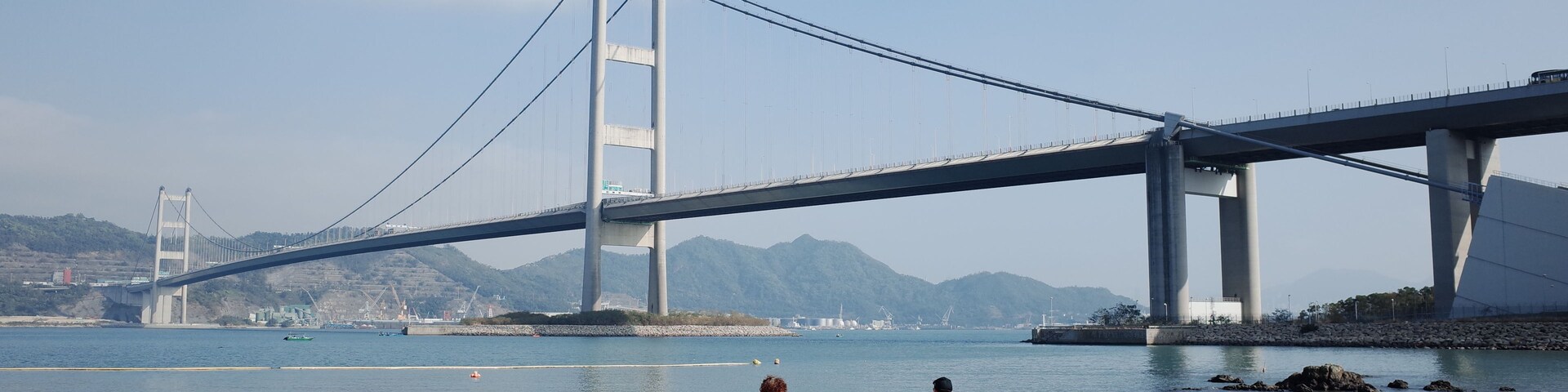Una playa con gente, un puente grande al fondo y montañas.