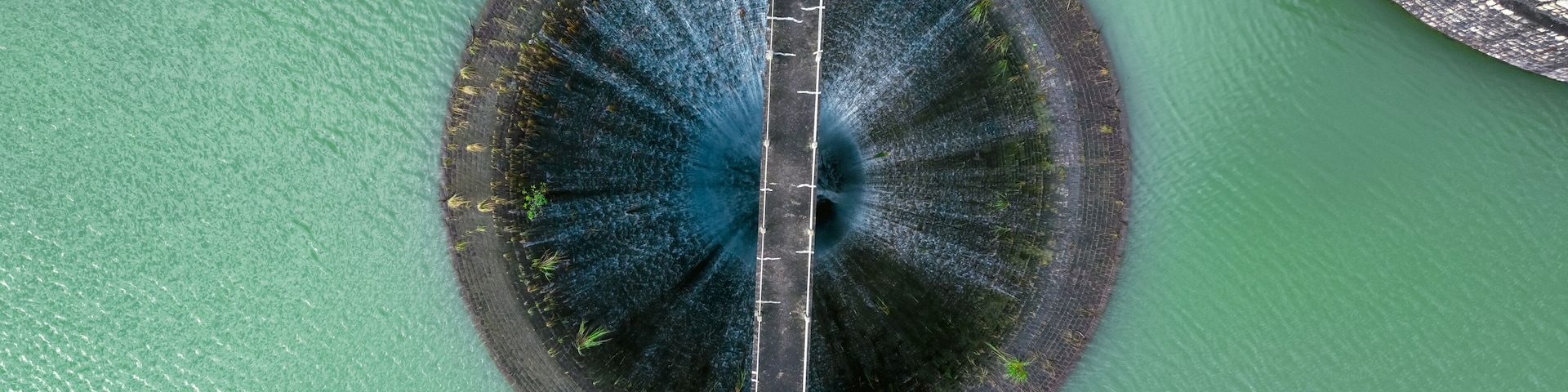 An aerial view of a circular water body with a central bridge.