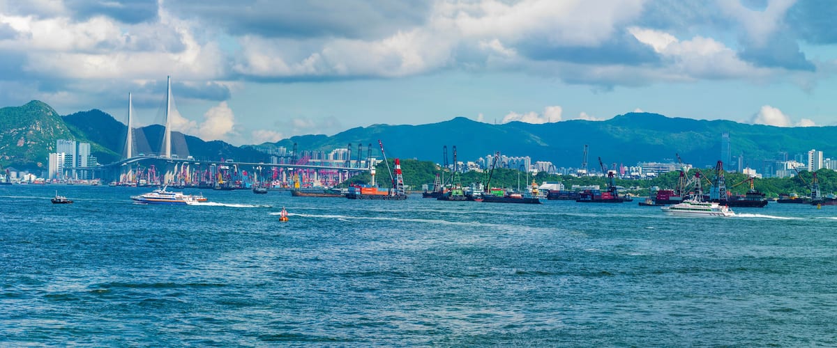 A coastal city with a prominent bridge, boats, and a mountainous backdrop.
