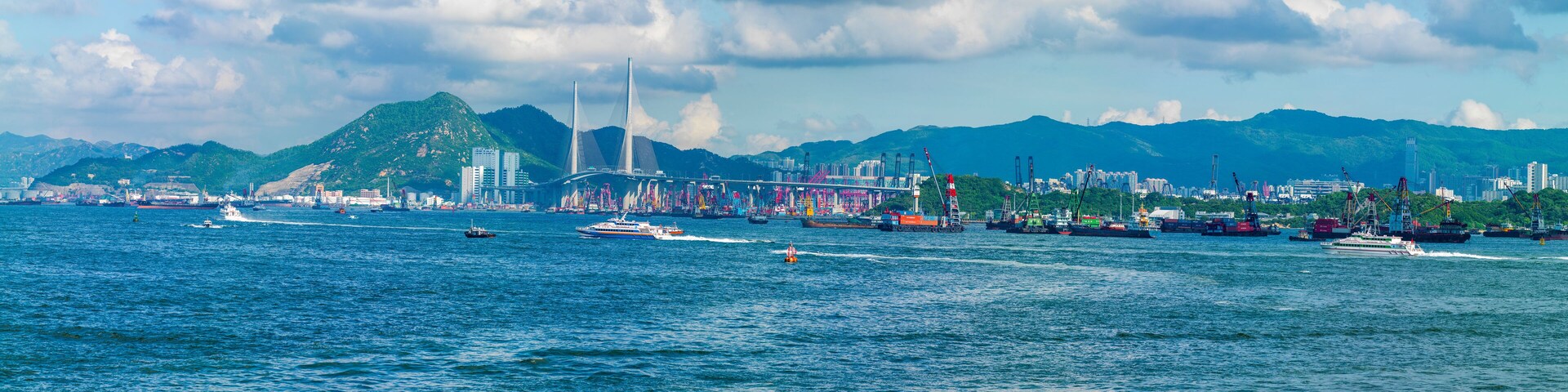 A coastal city with a prominent bridge, boats, and a mountainous backdrop.