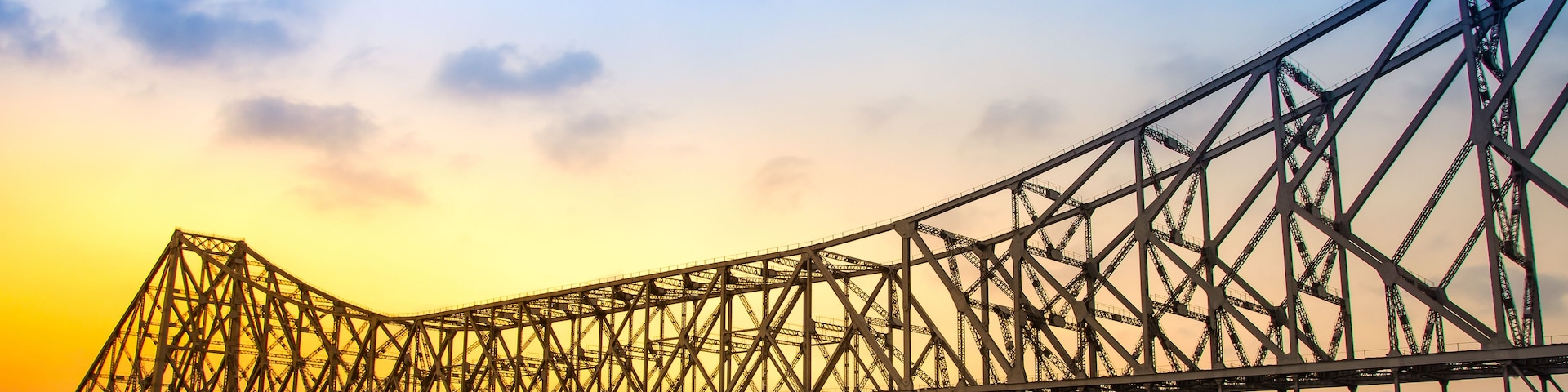 Un puente de acero imponente que cruza un río, con un atardecer en el horizonte.