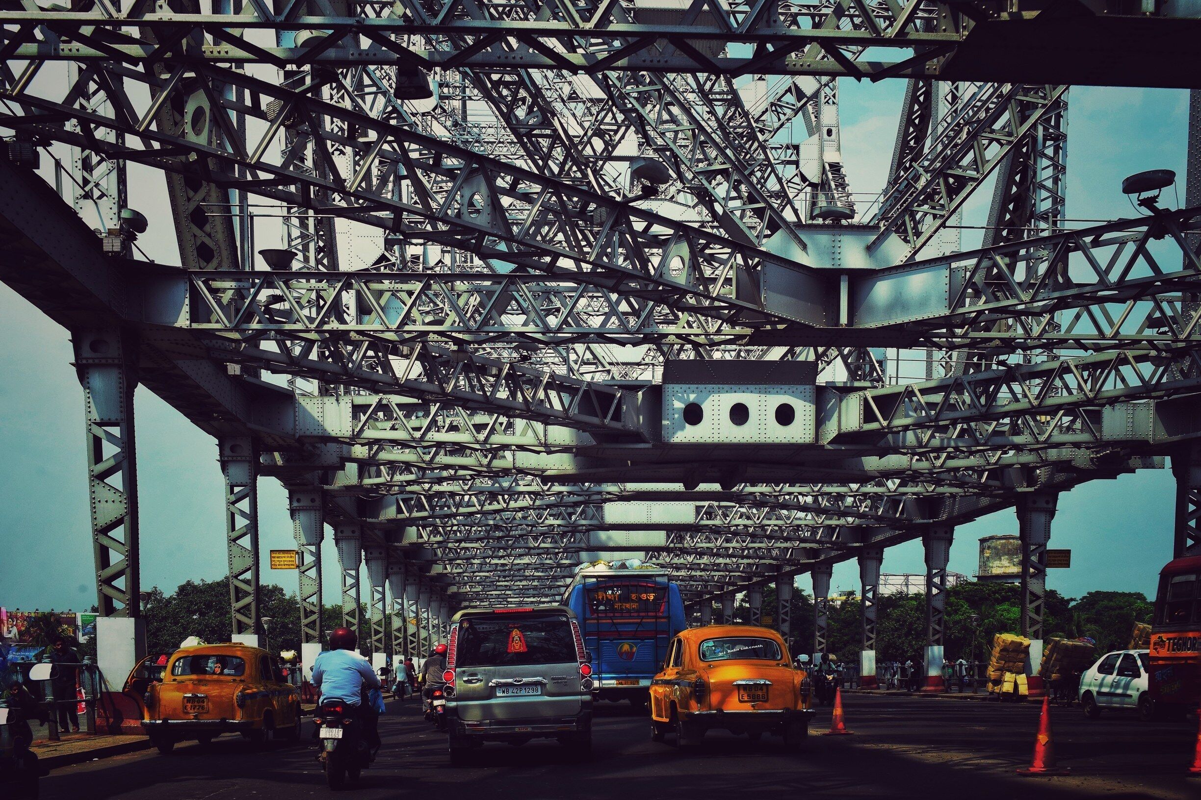 A busy toll booth with multiple vehicles, including cars and buses, passing through a metal bridge structure.