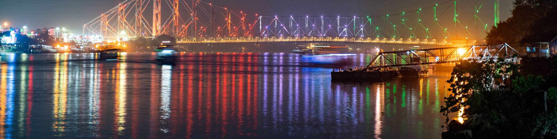 A nighttime view of a bridge with colorful lights reflecting on the water.