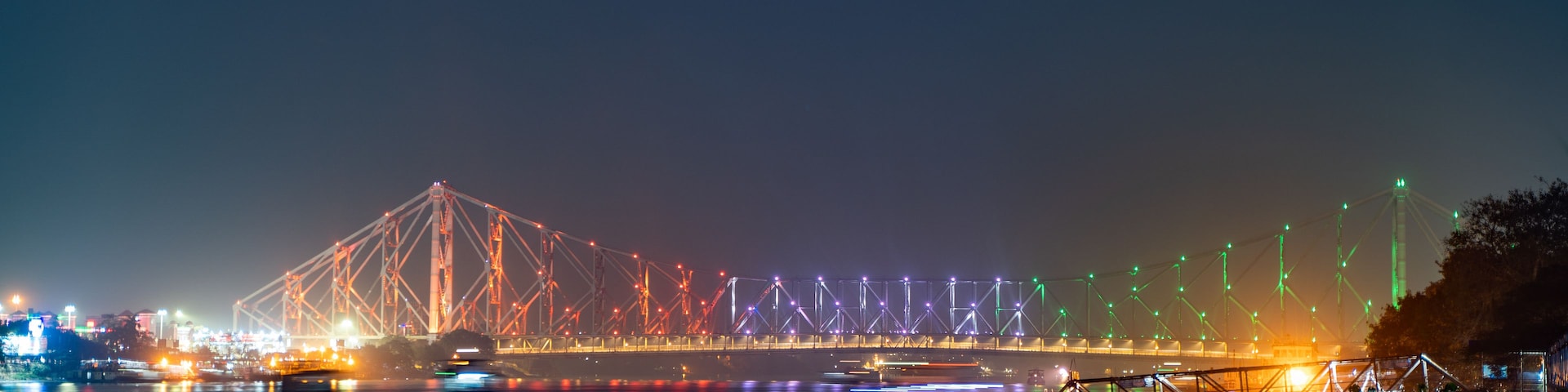 A nighttime view of a bridge with colorful lights reflecting on the water.