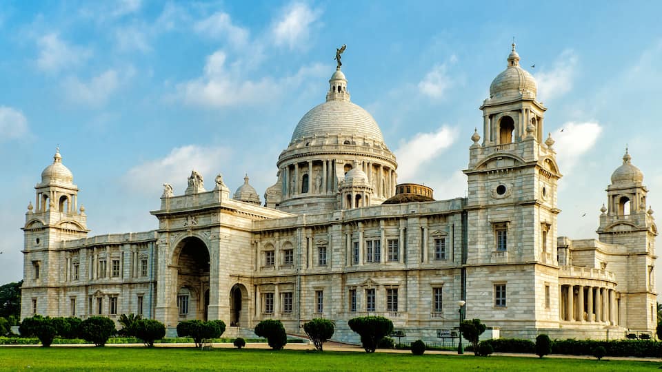 Un edificio grande e histórico con múltiples cúpulas y torres, rodeado de céspedes y árboles bien cuidados.