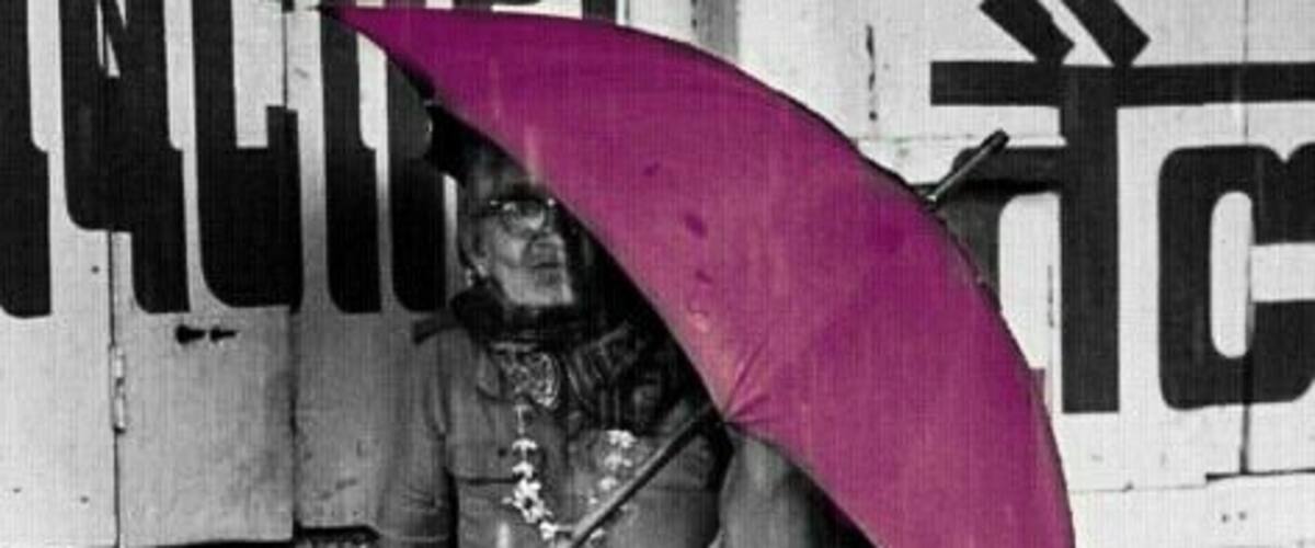 A person sitting on a concrete ledge by a body of water, holding a purple umbrella.