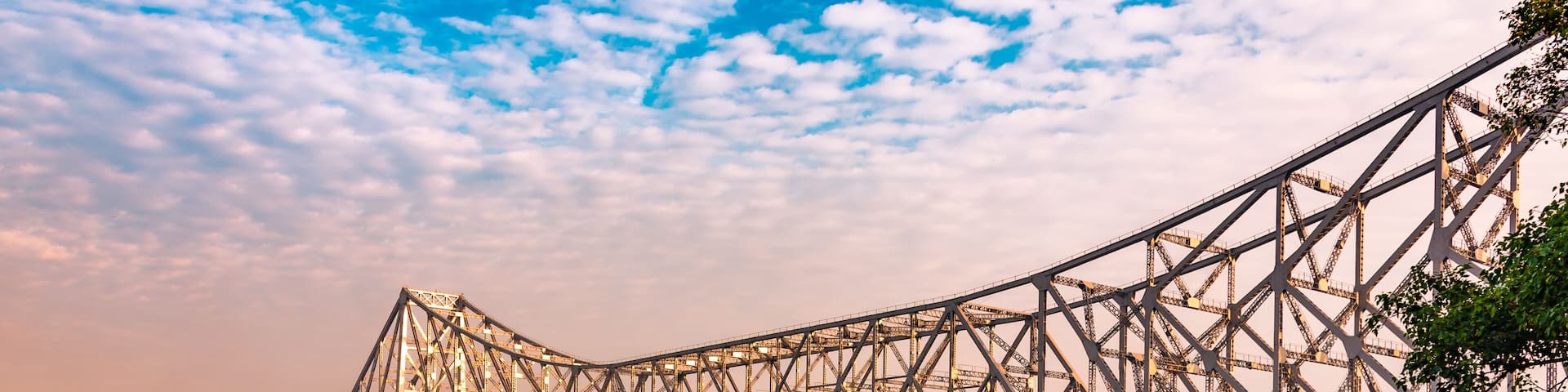 A large steel bridge spanning a river with a boat in the foreground and a cityscape in the background.