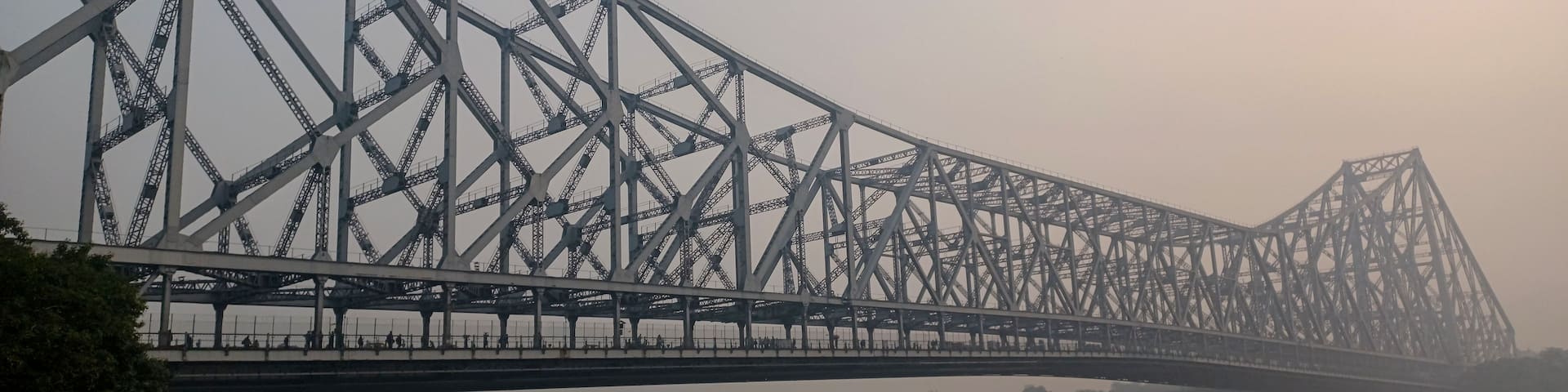 A large steel bridge spanning a river with a hazy sky.