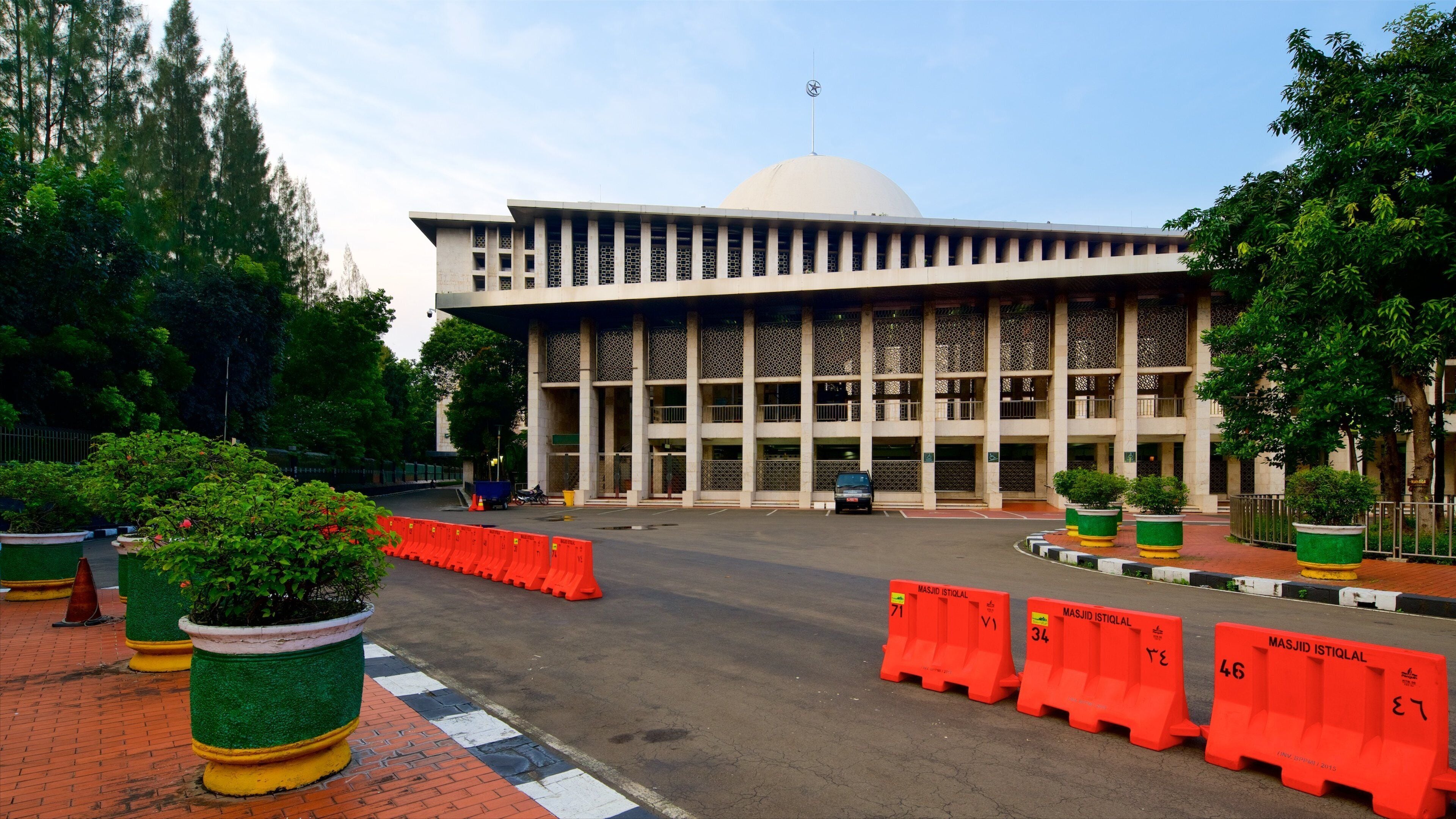 A large building with a dome and columns, surrounded by trees and potted plants.