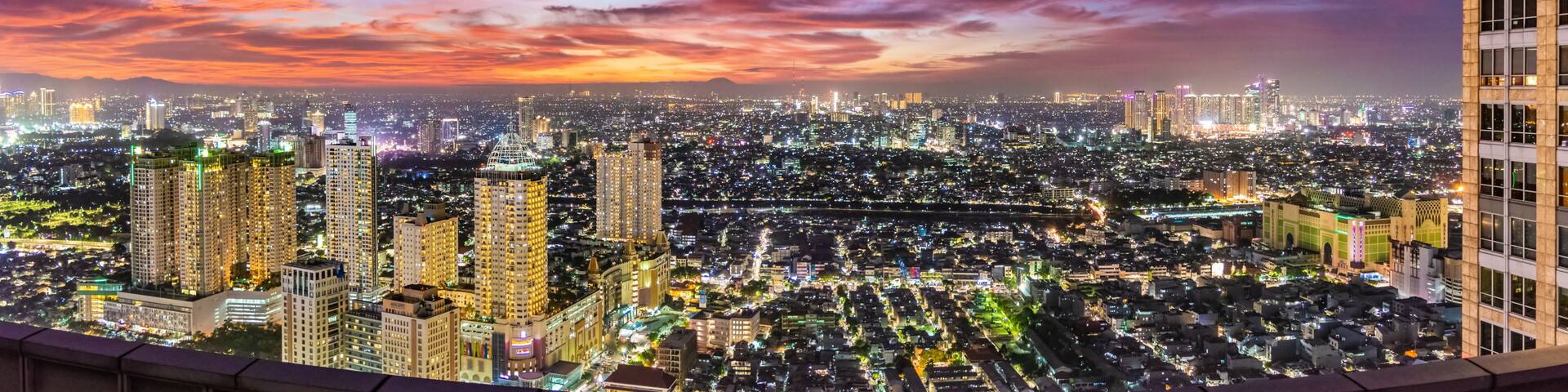 A cityscape at dusk with illuminated buildings and a colorful sky.