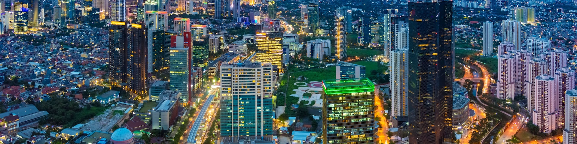 Paisagem urbana ao entardecer, com edifícios iluminados e traçado urbano denso.