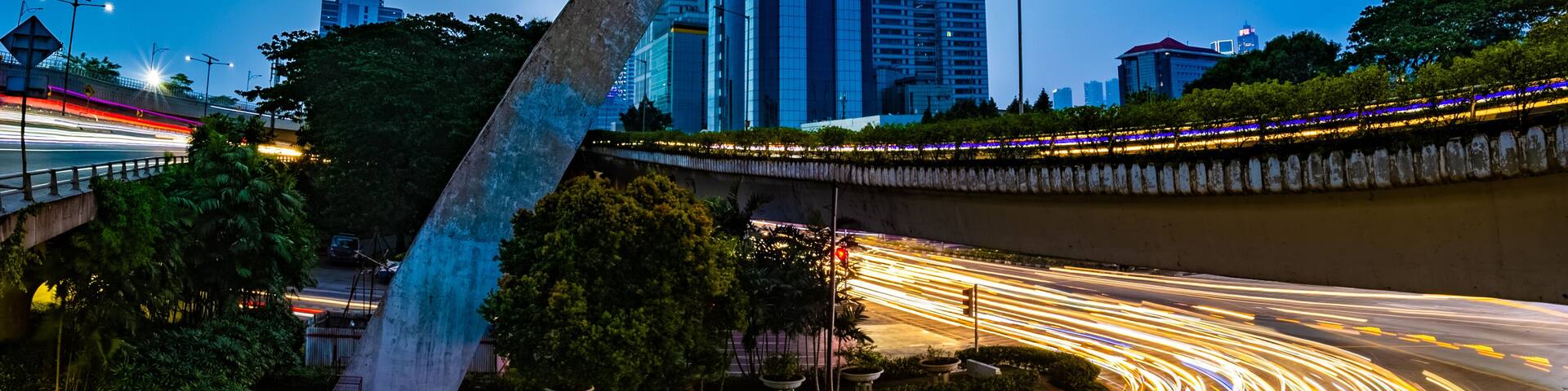A cityscape with a prominent sculpture, a curved road with light trails, and modern buildings.