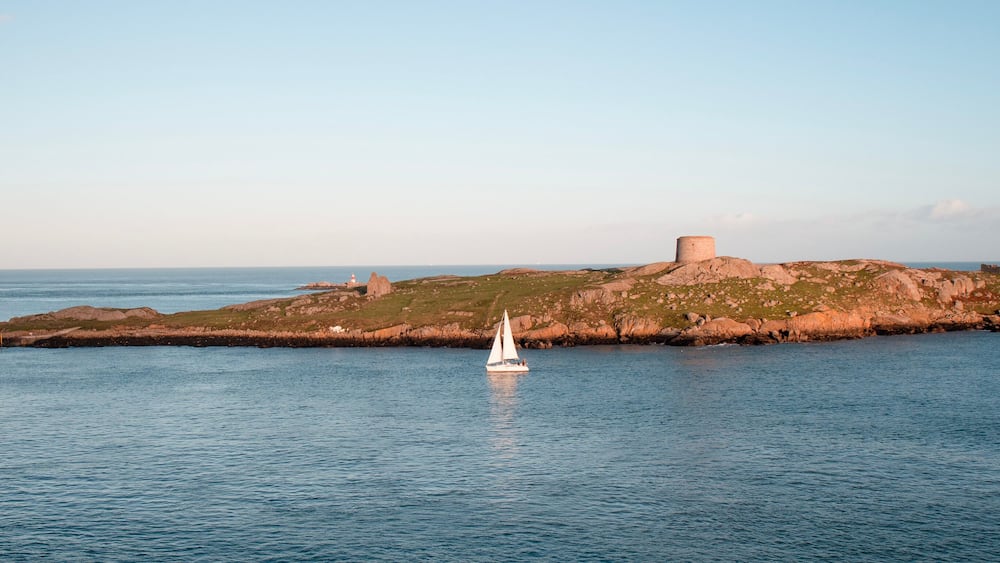 Dalkey, Ireland - Nov 5, 2022: View of Dalkey island and Saint Begnets Church ruins with a white yacht sailing by just before sunset