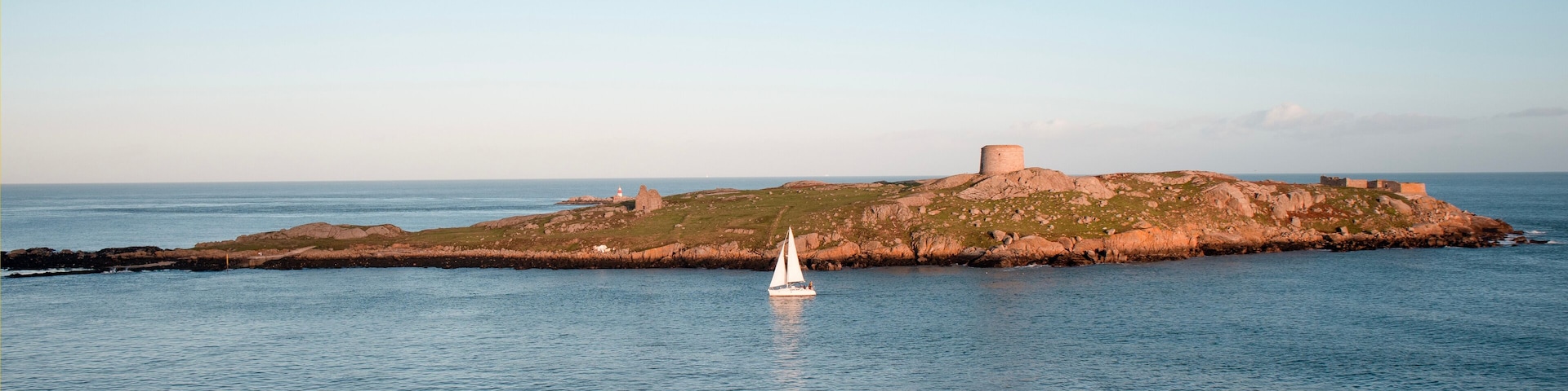 Dalkey, Ireland - Nov 5, 2022: View of Dalkey island and Saint Begnets Church ruins with a white yacht sailing by just before sunset