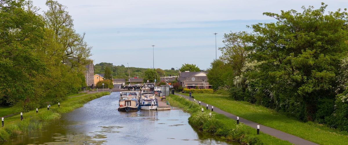A narrow waterway with boats, surrounded by greenery and buildings.