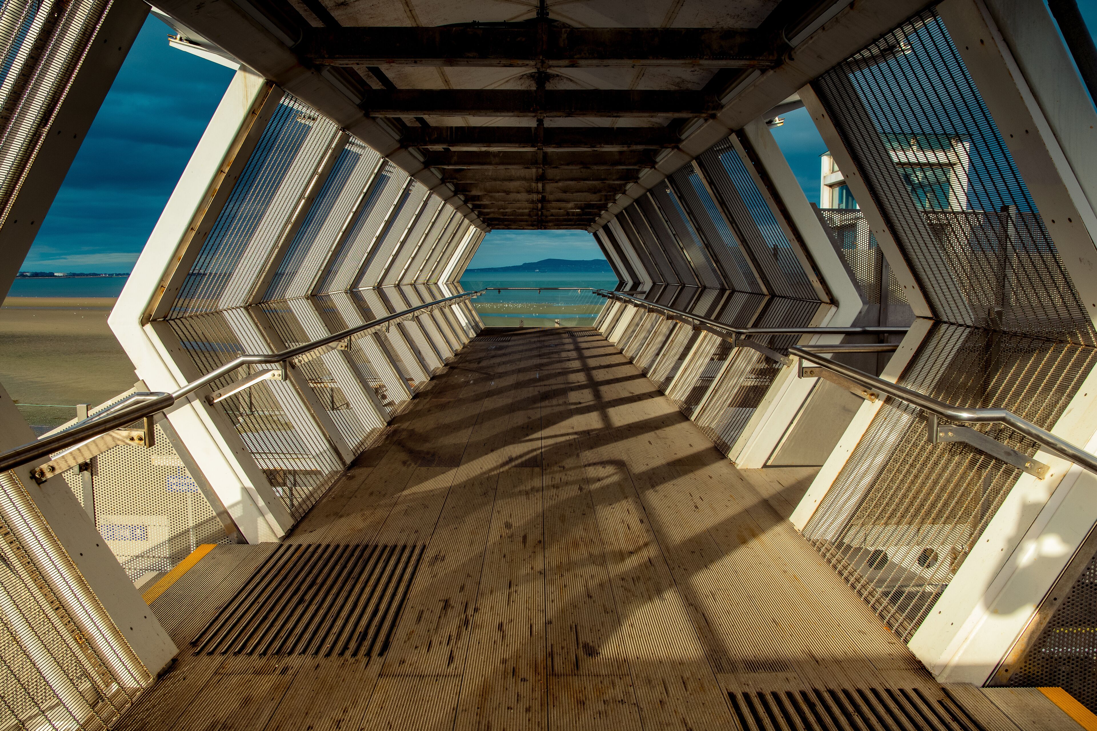 Modern polygon-shaped peatonal bridge in an Irish train station with a view at the beach.Booterstown dart station, Dublin, Ireland.