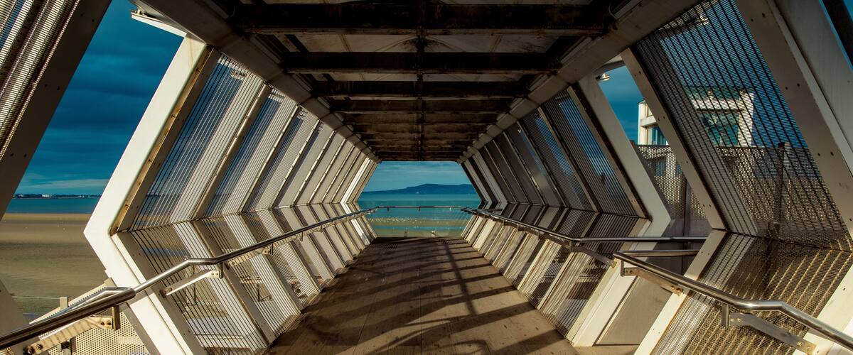 Modern polygon-shaped peatonal bridge in an Irish train station with a view at the beach.Booterstown dart station, Dublin, Ireland.